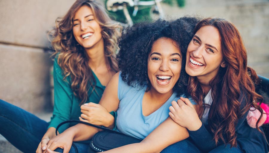 multicultural group of young women sitting and laughing outside showing healthy teeth and smiles