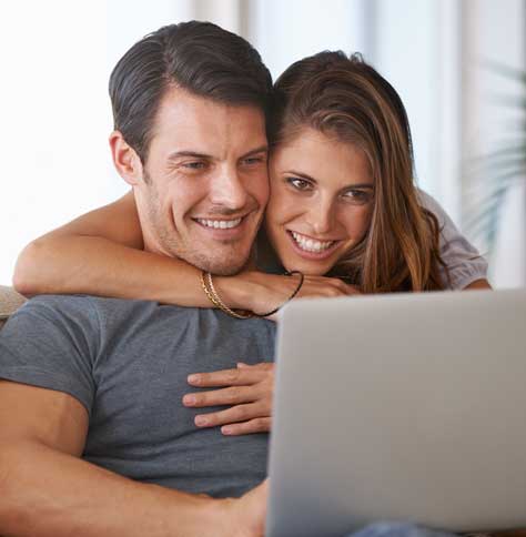 brunette man on laptop, brunette woman behind him, leaning over with arms around him