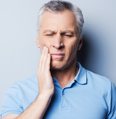 man with grey and white hair dealing with a toothache, touching cheek