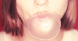 Close-up of lower half of brunette female face blowing a pink gum bubble against a red wall
