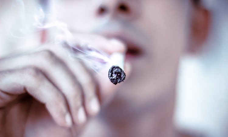 Closeup of a man smoking a cigarette that will discolor his teeth and cause oral cancer and bad breath