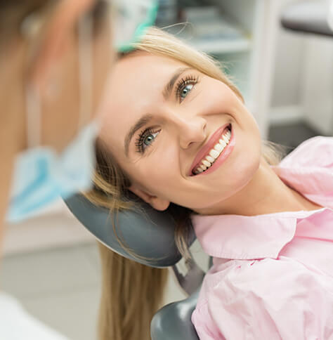 smiling, blonde woman lying in dental chair, speaking with her hygienist