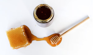 Aerial view of honey in a jar next to a honeycomb smothered in honey connected to a ridged wooden honey ladle