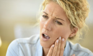 Closeup of a blonde woman touching her cheek due to painful dry socket