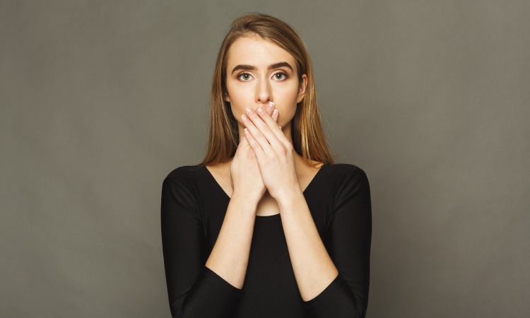  Une femme blonde portant une chemise noire se couvre la bouche avec ses mains parce qu'elle est gênée de son halitose 