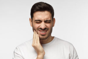 Dark-haired man cringing in pain and touching his cheek due to a toothache