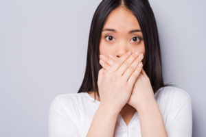 Dark-haired woman with bad breath covers her mouth with her hands in embarrassment