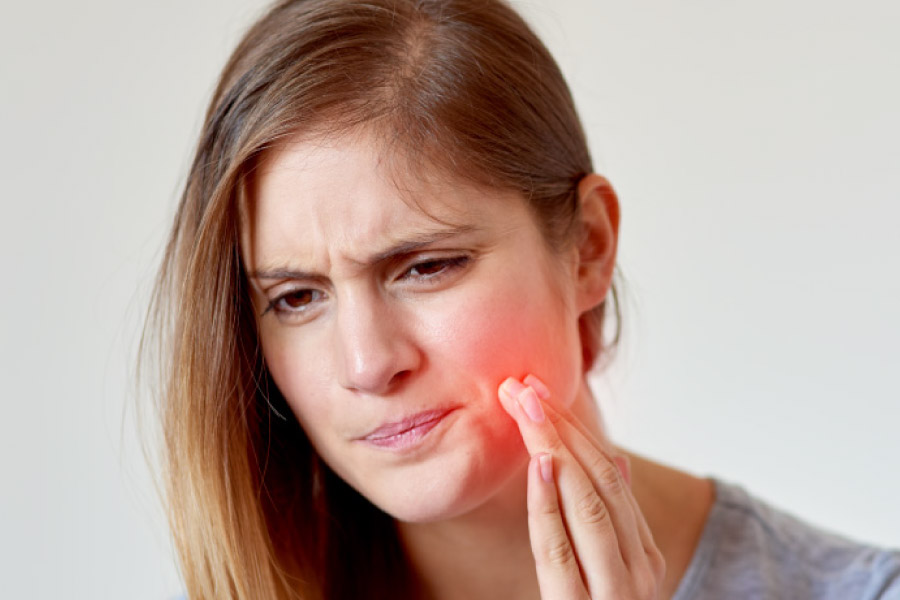 Blonde girl with her hand to her cheek and a pained facial expression due to a toothache.