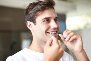 Young adult man smiles as he flosses his teeth.