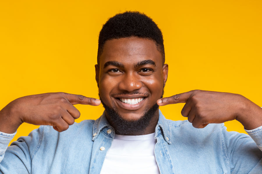 Smiling man pointing his fingers at his beautiful white smile.